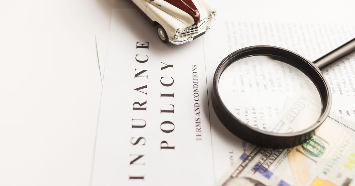 Close-up image of an insurance policy with a magnifying glass, money, and toy car.