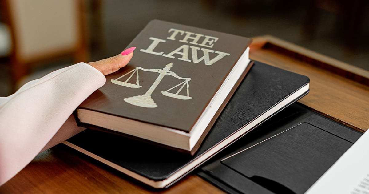 Closeup image of a law book titled 'The Law' on a wooden desk with scales of justice.