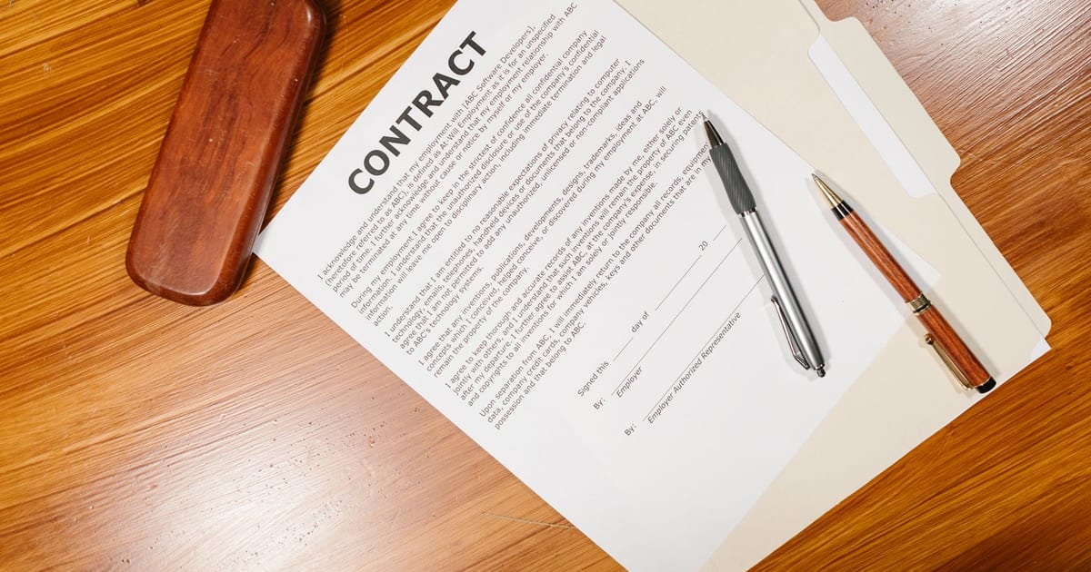 High-angle view of a contract document with pens and a case on a wooden table.