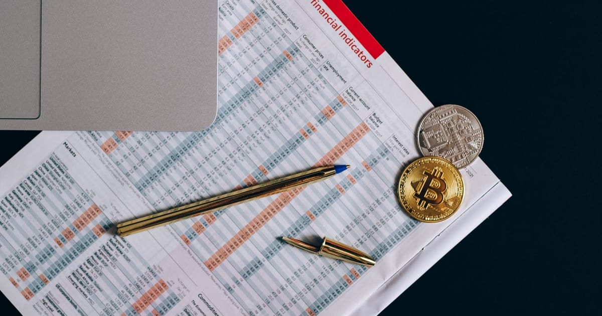 Top view of bitcoin coins on financial documents beside a laptop keyboard.