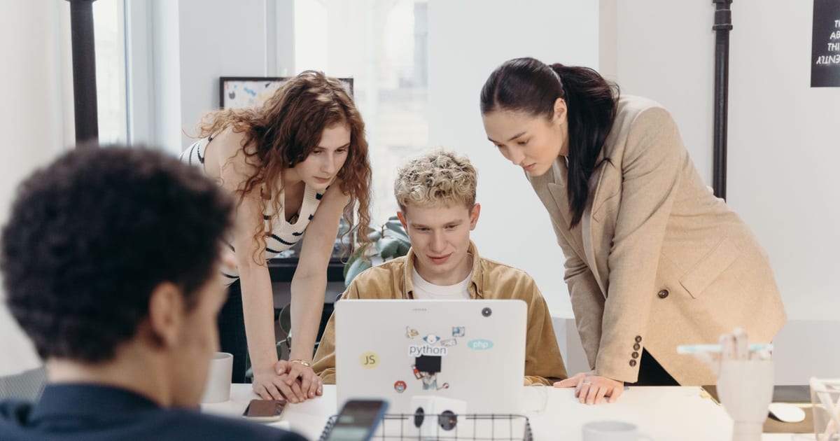 Three colleagues collaborate on a laptop, embodying teamwork and creativity in a modern office environment.