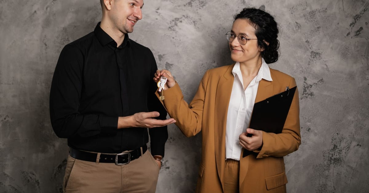 A real estate agent smiling as they hand over house keys to a new homeowner in an indoor setting.