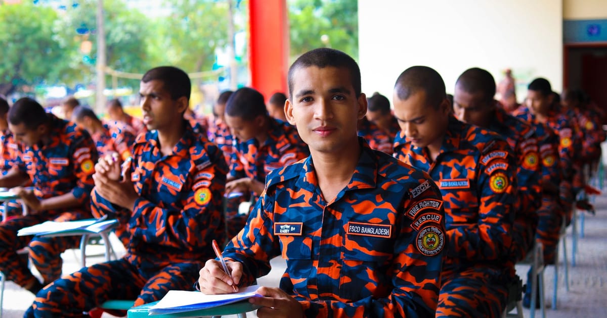 A group of firefighters in brightly colored uniforms attentively sitting and writing at a training session.
