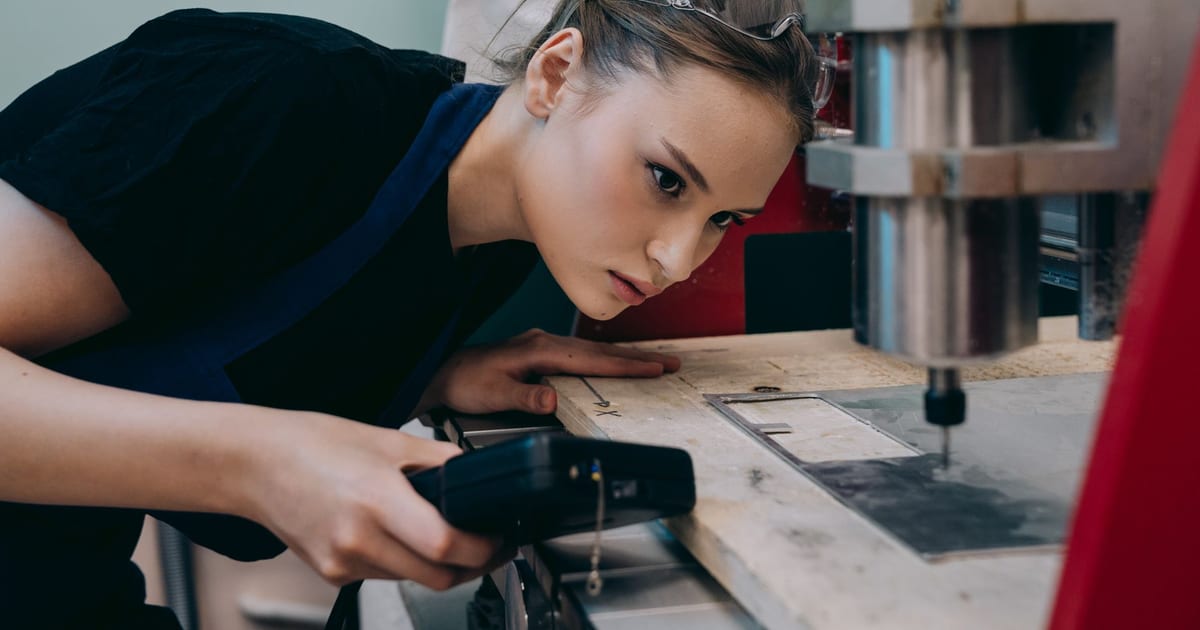 Woman closely inspecting machinery in a workshop wearing protective goggles.