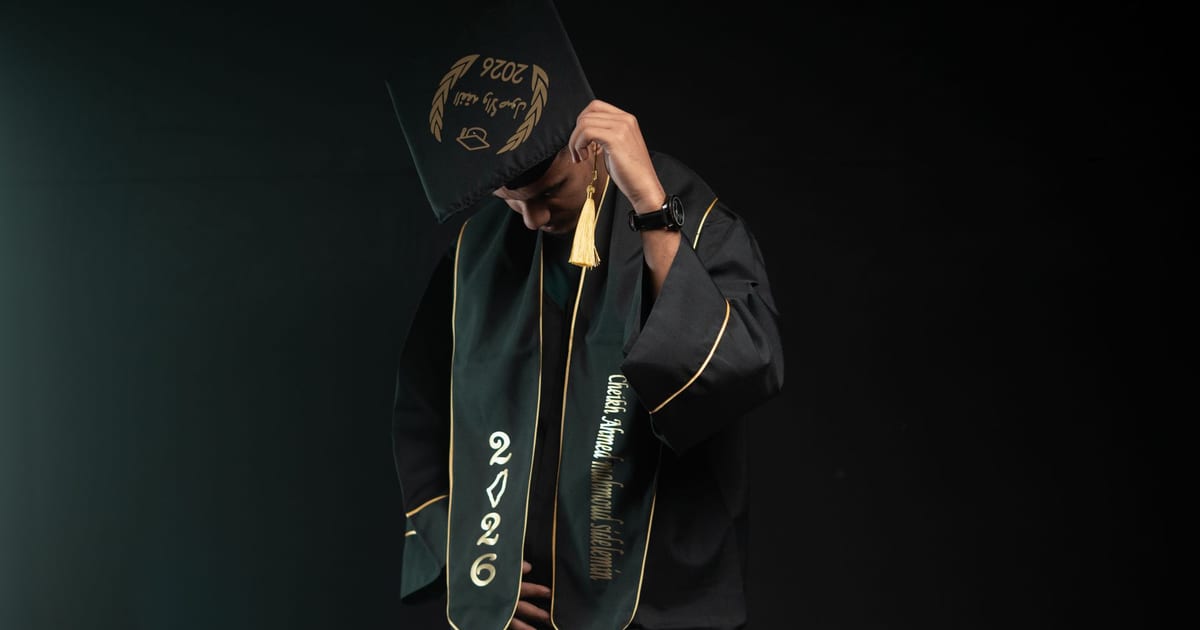 A graduate wearing a cap and gown, class of 2026, looking down in a studio setting.
