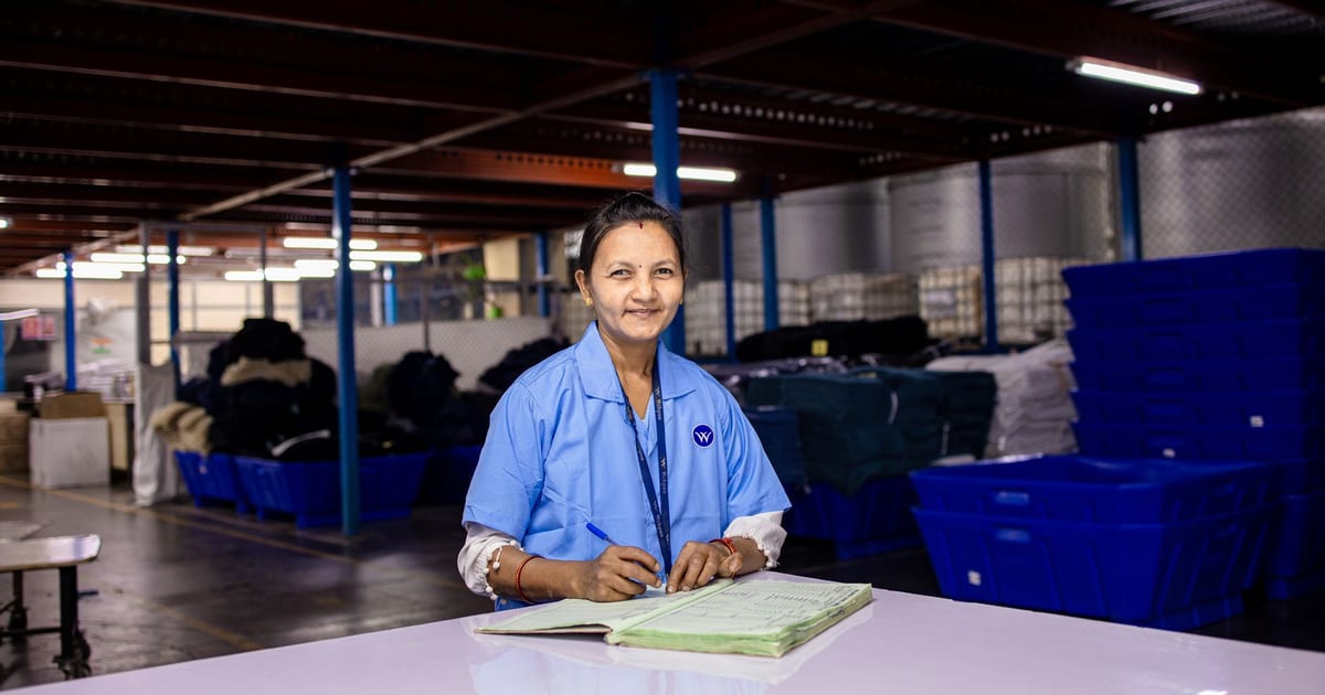 A woman in uniform writing in a notebook inside a textile warehouse.