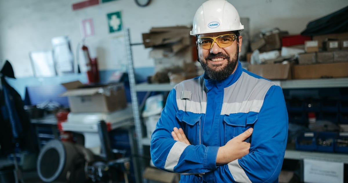 Smiling worker in blue uniform and hard hat standing in a factory setting in Russia.